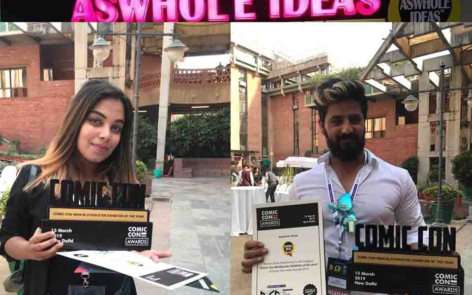 Image of Aswhole Ideas' booth at ComicCon India 2019: "Colorful display of fun and humorous products at Aswhole Ideas' booth at ComicCon India 2019" Image of Aswhole Ideas' Blockbuster Sale of the Year Award: "Aswhole Ideas' Blockbuster Sale of the Year Award trophy from ComicCon India 2019" Image of Aswhole Ideas' products: "Assortment of fun and humorous products from Aswhole Ideas, including fridge magnets, coasters, coffee mugs, and more"