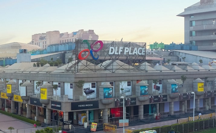 The image shows the storefront of Aswhole Ideas in DLF Saket Mall's Market Square ground floor. The store is brightly lit and has a colorful display of fun and humorous products in the window. A sign above the entrance displays the name of the store in bold, playful letters.